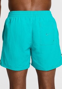Pantaloni da bagno turchesi realizzati in tessuto leggero. Caratterizzati da una cintura elastica, tasche laterali e una tasca posteriore con il logo Nike.