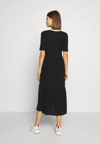 Svart midi-kjole laget av lett stoff, med korte ermer, lagdelt skjørt og en avslappet passform. Kombinert med hvite joggesko.