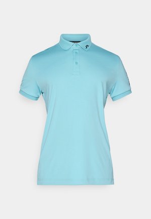 Světle modré polo tričko vyrobené z měkké tkaniny, s klasickým límečkem, zapínáním na tři knoflíky a jemným logem na hrudi. Krátké rukávy.