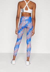 Legginsit, joissa on sininen pohja, geometriset punaiset ja valkoiset kuviot, korkea vyötärö, yhdistetty valkoisen urheilutuotteen kanssa. Pehmeä, joustava kangas.