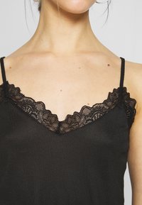 Camisola nera con un bordo in pizzo floreale lungo la scollatura a V e sottili spalline regolabili, realizzata in un morbido tessuto a coste.