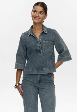 Top in denim con colletto, maniche a tre quarti e chiusura a bottoni. Presenta una tasca frontale e una vestibilità cropped. Lavaggio blu scuro.