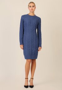 Vestito a maglia multicolore blu, con un motivo a rombi, maniche lunghe e orlo a coste. Abbinato a scarpe con tacco nere.