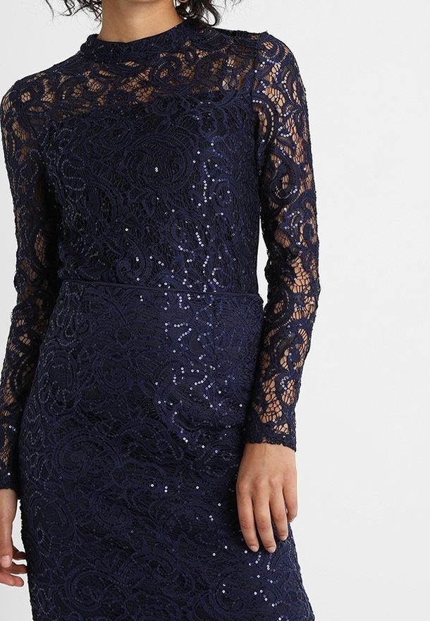 Marinblå spetsklänning med långa ärmar, som har intrikata blommönster och paljetter för textur. Hög halsringning och figurnära design.
