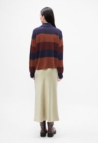 Pull en tricot à rayures bleu marine, rouille et violet foncé, associé à une jupe maxi en satin crème et des bottines marron, vu de dos.