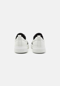 Baskets blanches en cuir avec un accent noir au talon, dotées d'une épaisse semelle blanche et d'un logo "Calvin Klein" discret à l'arrière.