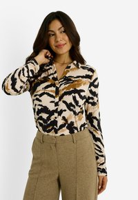 Camisa de manga larga con botones que presenta un diseño de estampado animal abstracto en tonos beige, negro y marrón. Tejido suave con cuello tipo solapa.