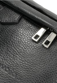Černá kabelka z strukturované kůže s klopovým uzávěrem a dvojicí zipů ve stříbrném odstínu, s texturovaným povrchem a decentním logem.