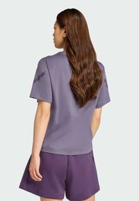 Lila bomullströja med korta ärmar, rund halsringning och en mjuk textur. Tillsammans med mörklila träningsshorts.