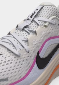 Chaussure de course Nike en mesh blanc avec le logo Swoosh noir, des accents roses et orange, et une étiquette "WUNFLO 12" sur la languette avec des lacets blancs.