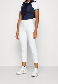 Sportkläder med en figursydd marinblå och vit topp med logodetaljer, vita stretchbyxor och vita sportskor.