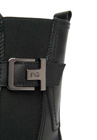 Stivale nero con un pannello in tessuto texturizzato e dettagli in pelle liscia. Nota caratteristica è la fibbia metallica con lettere incise.