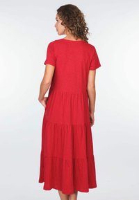 Rotes, kurzärmliges Kleid mit einem gestuften Design. Weicher, strukturierter Stoff. Fällt bis zur Mitte der Waden mit einem runden Ausschnitt.