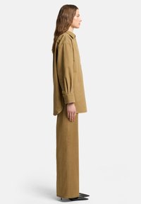 Za duża beżowa koszula z miękkiego materiału, zapinana na guziki, z długimi rękawami. Połączona z dopasowanymi szerokimi spodniami i eleganckimi czarnymi szpilkami.