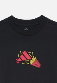 Μαύρο βαμβακερό T-shirt με γραφικό κόκκινων πατατών σε δοχείο με κίτρινες λεπτομέρειες και λογότυπο Adidas. Στρογγυλή λαιμόκοψη και κοντά μανίκια.