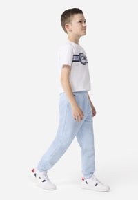 Biele tričko s krátkym rukávom s modrou grafikou a horizontálnymi pruhmi, v kombinácii s svetlomodrými teplákmi a bielymi teniskami s akcentmi.