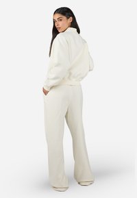 Set aus ivoryfarbenem Sweatshirt und Hose, gefertigt aus weichem Stoff. Das Oberteil hat einen hohen Kragen und einen gerippten Saum; die Hose verfügt über Seitentaschen und einen lockeren Schnitt.