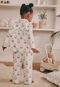 Ensemble de pyjama pour enfants en tissu blanc orné d'imprimés colorés de lapins. Haut ample à manches longues et pantalon assorti. Matière douce et texturée.