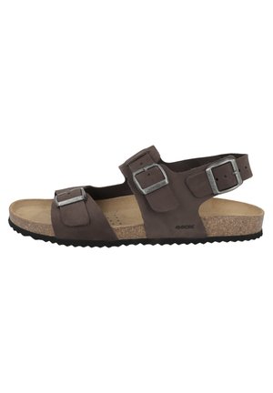 Sandalo marrone in suede con due cinturini regolabili e fibbie in metallo. Soletta in sughero e suola in gomma nera testurizzata per una buona aderenza.