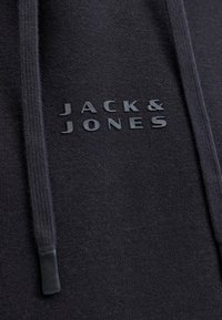 Nahaufnahme von schwarzem Hoodie-Stoff mit schwarzem "JACK & JONES"-Logo und passenden schwarzen Kordeln mit Kunststoffspitzen.