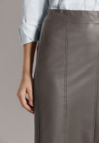 Grijze leren kokerrok met zichtbare stiksels, met een hoge taille en een gladde textuur. De hand van het model rust lichtjes op de stof.