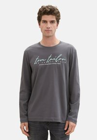 Gray long-sleeve t-shirt in cotton blend with a crew neck, featuring white and teal text on the front. Simple, relaxed fit design.