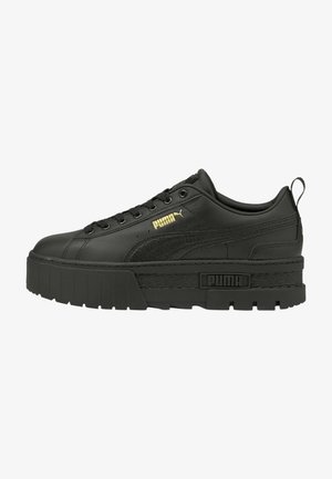 Zapatilla negra de Puma con suela gruesa y texturizada, parte delantera con cordones, logo dorado de Puma en el lateral y una pestaña en el talón, mostrada en perfil lateral.