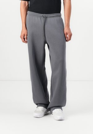 Grå vid ben sweatpants laget av mykt stoff, med elastisk midje og snor. Brukes med hvite treningssko.
