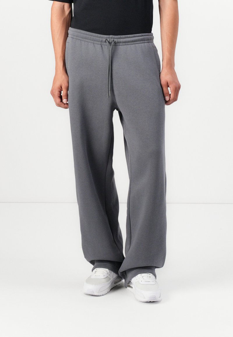 Gray wide-leg sweatpants made of soft fabric, featuring an elastic waistband with a drawstring. Worn with white athletic shoes.
