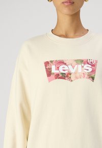 Krémová mikina s květinovým logem Levi's v růžové a bílé barvě. Tkanina má měkkou strukturu a uvolněný střih.