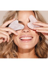 Two heart-shaped, translucent rose quartz stones held against a person's eyes, featuring a smooth surface and subtle marbling.