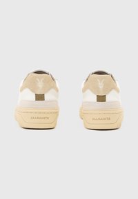 Baskets blanches avec des accents en daim beige, dotées d'une semelle texturée, d'un onglet au talon portant une marque et d'un design minimaliste.