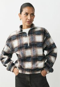 Fleece pullover med lynlås krave, med et ternet mønster i nuancer af marineblå, hvid og burgunder. Ribbet kant og manchetter.