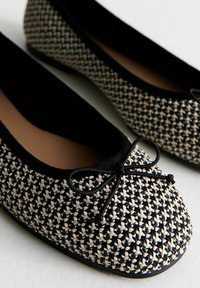 Ballet flats intrecciati in bianco e nero con parte superiore texturizzata, punta arrotondata e fiocco decorativo sul davanti. Fodera interna morbida e suola flessibile.