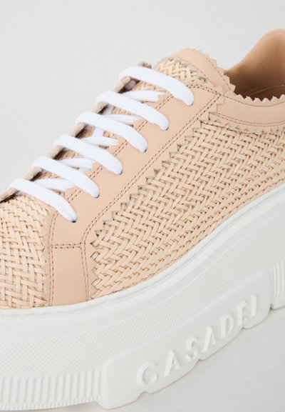 Beige woven leather sneaker with white laces, raised rubber sole, and textured detailing on the upper. Brand name embossed on sole.