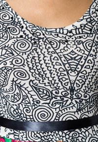 Materiał w wielu wzorach z czarnymi abstrakcyjnymi zwojami i liśćmi na białym tle, z czarną wstążką jako akcentem w talii.