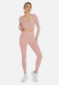 Conjunto de activewear rosa claro que incluye una camiseta corta de manga larga con escote cuadrado y leggings de talle alto a juego. Marca sutil en blanco.
