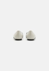 Ballerines en cuir gris clair avec un bout arrondi, une texture lisse et un design minimaliste. Semelle extérieure noire plate et sans quincaillerie visible.