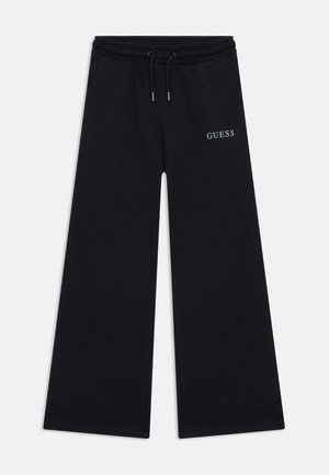Calças de moletom pretas feitas de um tecido macio, com um design de perna larga, cintura elástica com cordão e o logótipo "GUESS" bordado em branco.