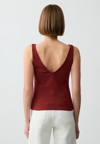 Canotta a costine color bordeaux con scollo a V. Presenta spalline sottili e una silhouette aderente, abbinata a pantaloni bianchi a vita alta.