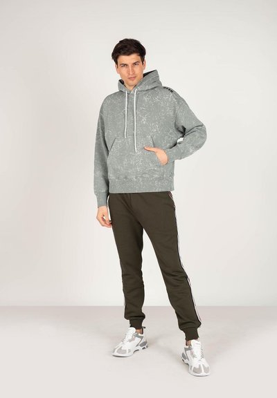 Szara bluza z kapturem o fakturowanym wzorze i przednią kieszenią, zestawiona z oliwkowymi dresami z bocznymi paskami. Model nosi szare i białe sneakersy.