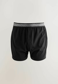Schwarze Baumwoll-Boxershorts mit einem gemusterten weißen elastischen Bund und einem Frontknopfverschluss. Glatte Textur, lockere Passform.