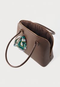 Καφέ δερμάτινη τσάντα χειρός με φερμουάρ, δύο χερούλια και ένα διακοσμητικό μπρελόκ με μαντήλι που έχει γεωμετρικό σχέδιο σε πράσινο και μπλε.