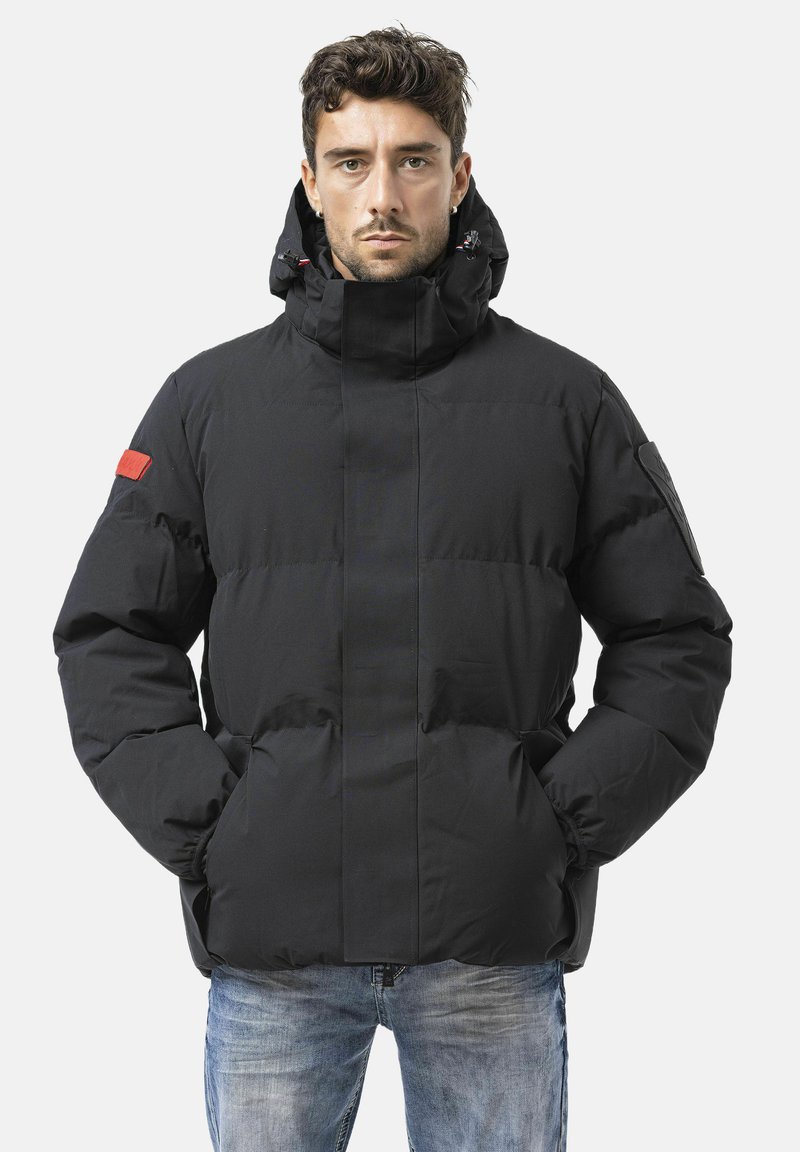 Schwarze, wattierte Jacke mit hochgestelltem Kragen, sichtbaren Nähten, einem roten Akzent am linken Ärmel und einer glatten, matten Oberfläche.