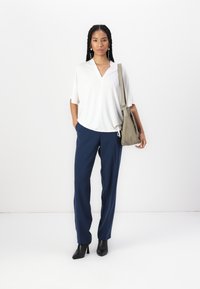 Witte, korte mouwen, V-hals top gecombineerd met marineblauwe, rechte broek. Zwarte haklaarzen en een grijze tas maken de outfit compleet.
