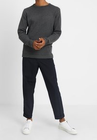 Pull gris foncé en maille avec un col rond, associé à un pantalon fuselé bleu marine et des baskets blanches. Éléments de design simples et texturés.