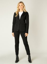 Zwarte blazer met notch-lapels, twee voorzakken en een enkele knoopsluiting, gecombineerd met zwart aansluitende broek en enkellaarsjes.