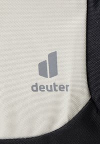 Deuter-logo på et teksturert stoff, med en svart og lysegrå fargekombinasjon, der merkevarenavnet er trykt i grått.