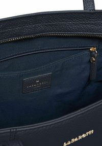 Interior de un bolso de mano de cuero azul oscuro que muestra un bolsillo con cremallera y tirador de cremallera en color dorado, con la etiqueta de la marca "Lazarotti" cosida en el interior.