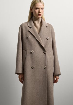 Cappotto in lana marrone chiaro doppio petto con grandi bottoni, rever a punta e tasche laterali. Tessuto morbido e vestibilità oversize.